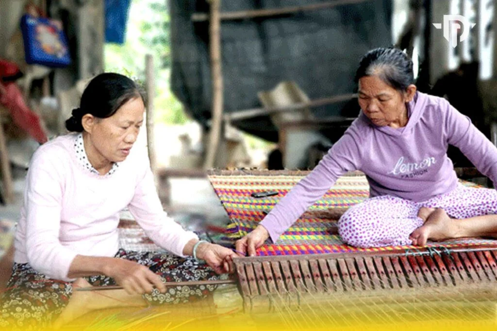 Hai người thợ phối hợp bên khung dệt chiếu hoa
